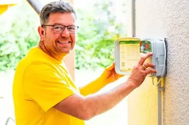 Mann in gelbem T‑Shirt bedient einen Stromzähler an der Hauswand